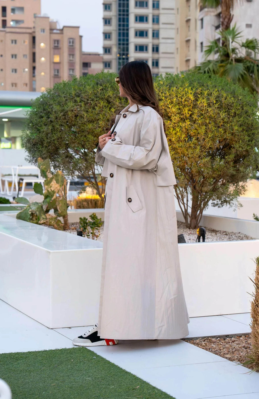 Beige Sandline chino trench coat with wide storm flap, front buttons, and flap pockets in relaxed fit for layering over casual or abaya outfits