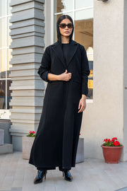 Woman wearing Veluxe black velvet and crepe abaya with blazer cut and structured lapels, standing outdoors.