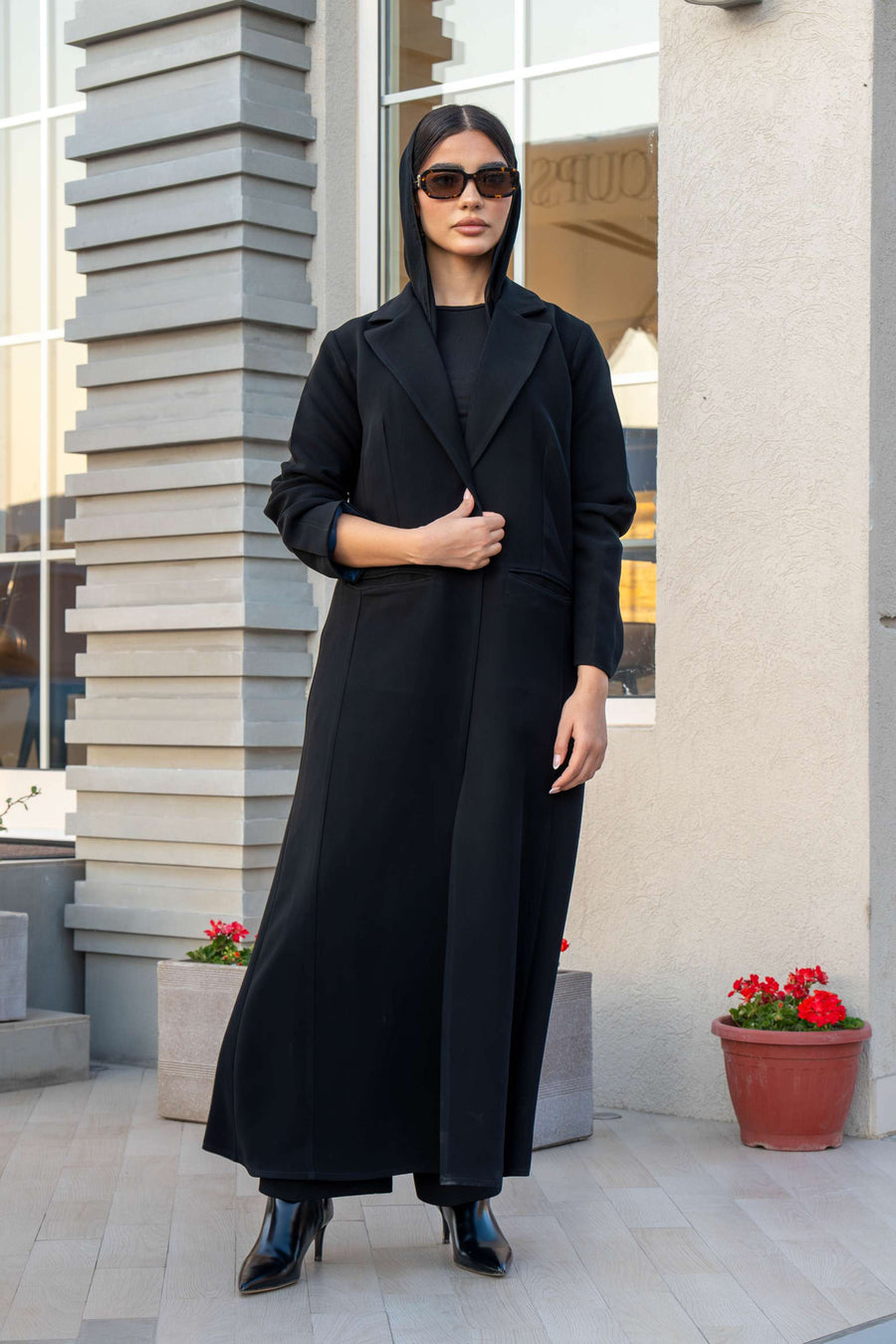 Woman wearing Veluxe black velvet and crepe abaya with blazer cut and structured lapels, standing outdoors.