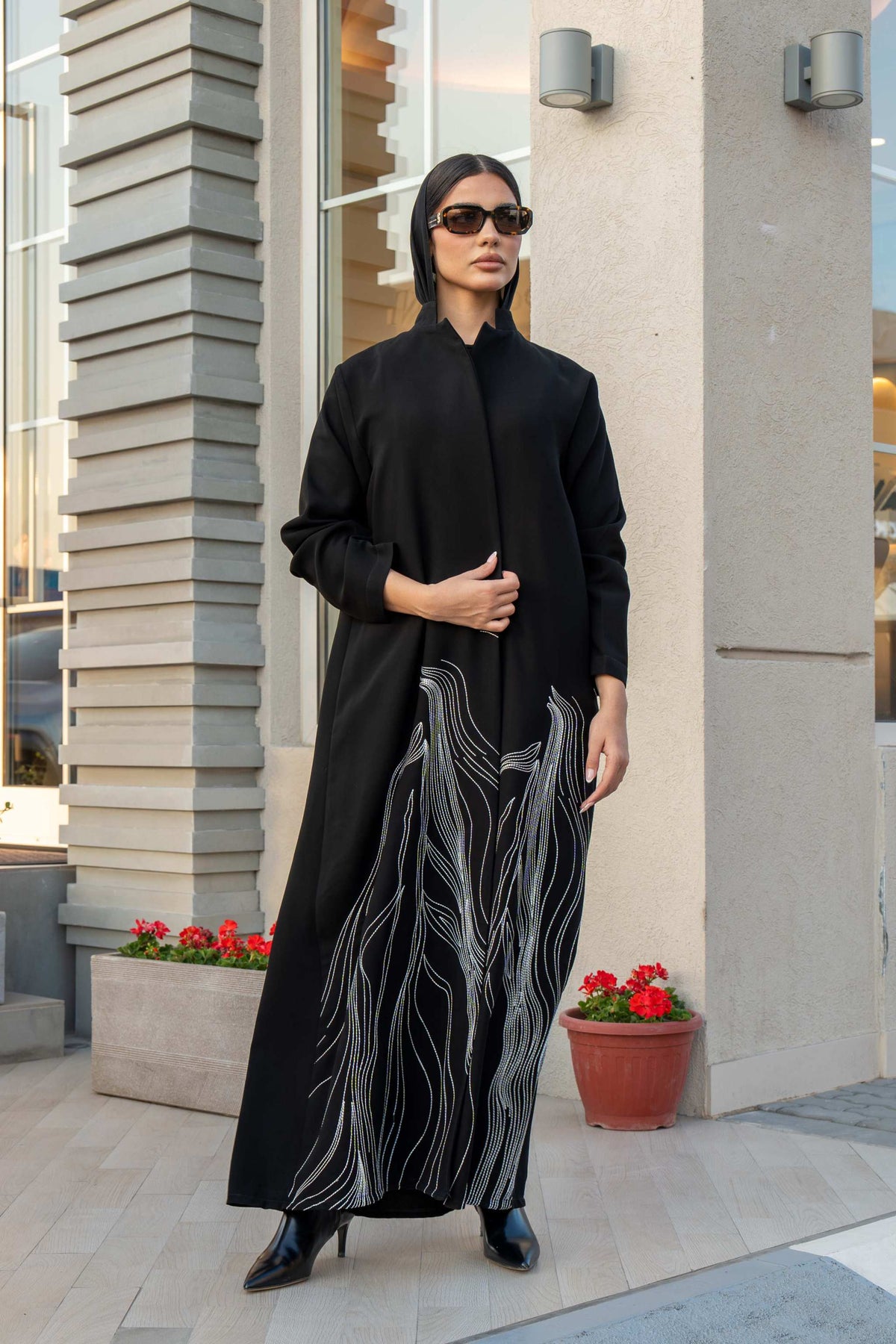 Woman wearing black crepe abaya with white shak embroidery along lower edges, standing outdoors.