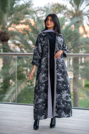Woman wearing a black and gray jacquard abaya with textured weave and soft chiffon lining, standing outdoors.