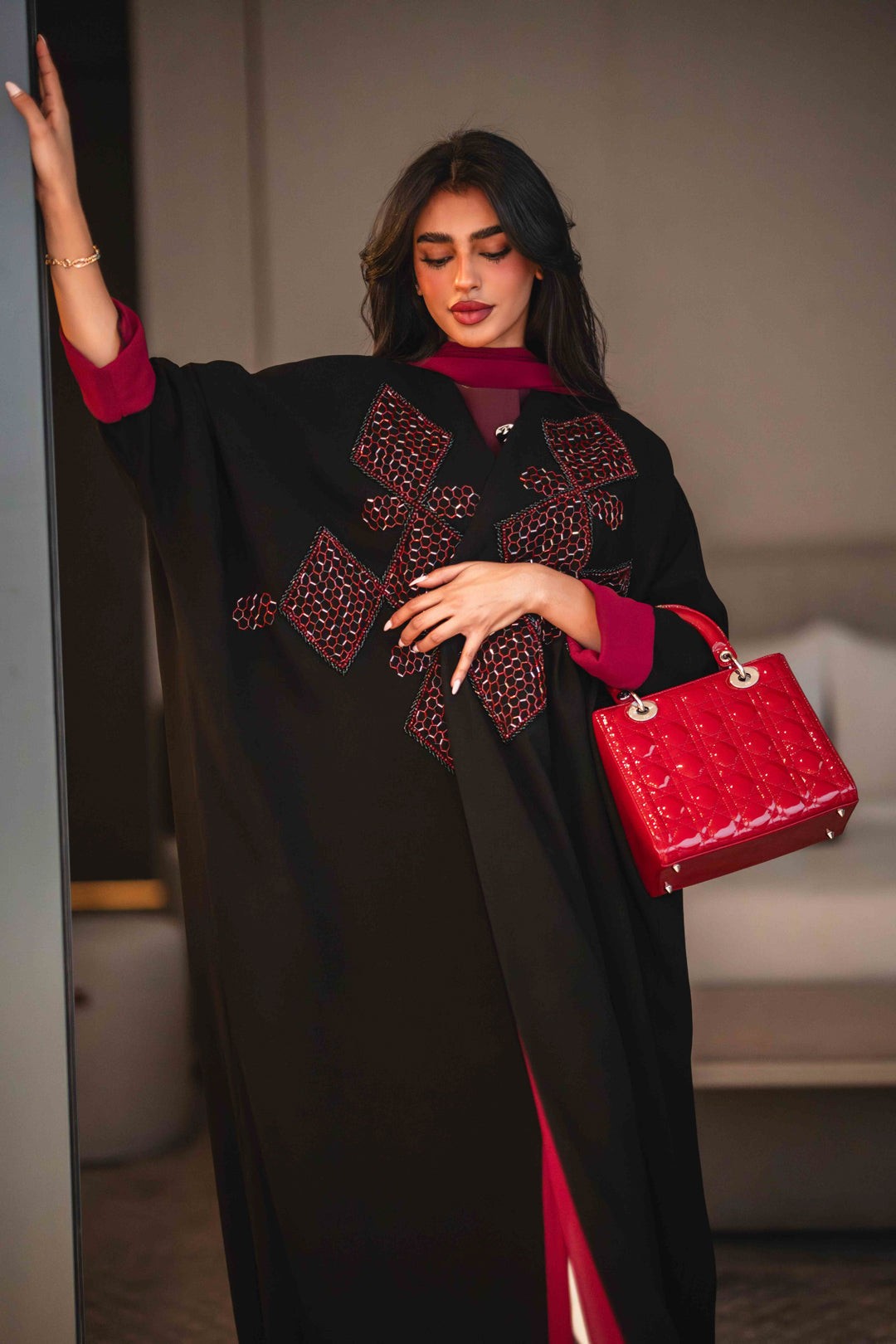 Black crepe abaya with bold red geometric embroidery and wide sleeves, styled with a matching red inner lining and red handbag.