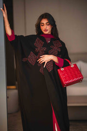 Black crepe abaya with bold red geometric embroidery and wide sleeves, styled with a matching red inner lining and red handbag.