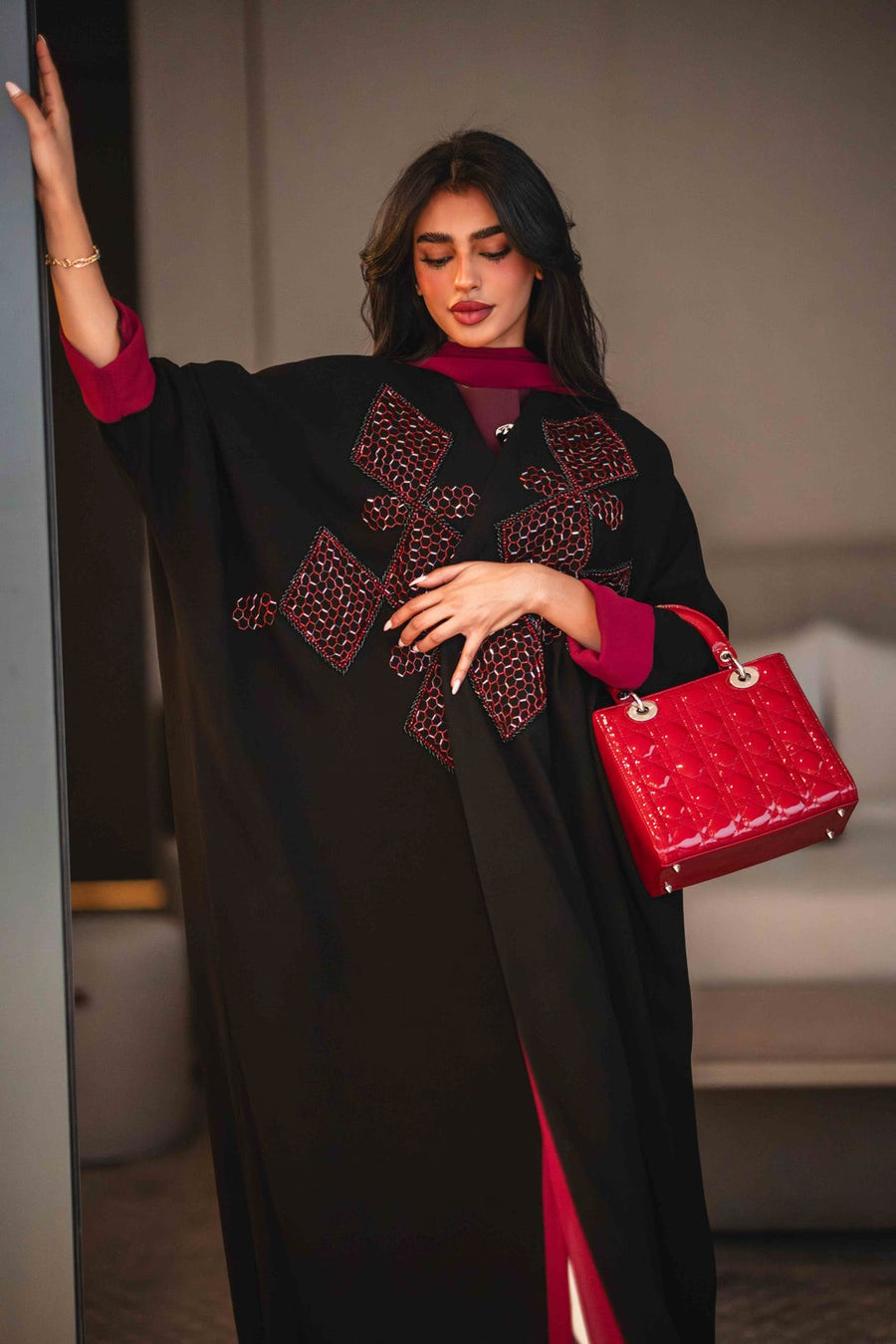 Black crepe abaya with bold red geometric embroidery and wide sleeves, styled with a matching red inner lining and red handbag.