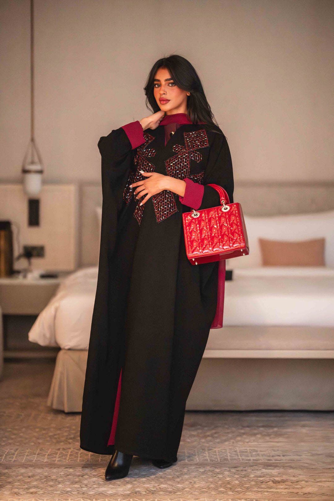 Black Ruby black crepe abaya with bold red geometric embroidery and wide sleeves, styled with a red inner lining and matching red handbag.