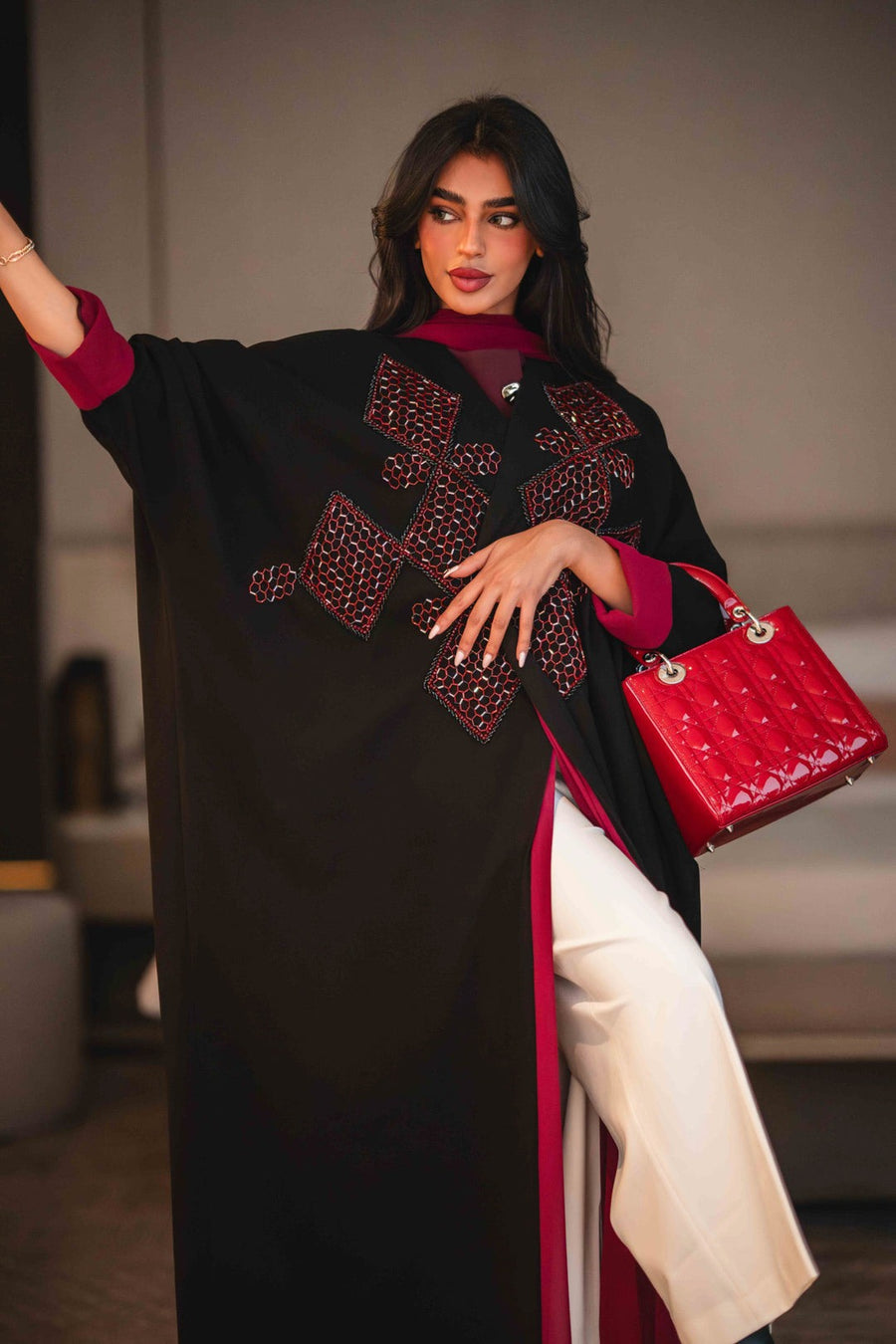 Black Ruby black crepe abaya with bold red geometric embroidery and wide sleeves, styled with a red inner lining and matching red handbag.