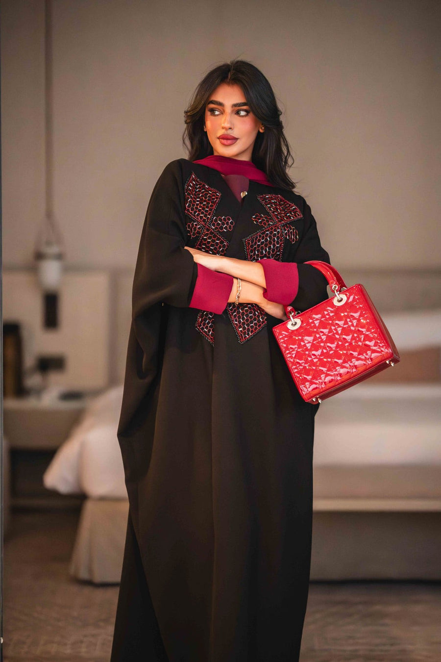 Black Ruby black crepe abaya with bold red geometric embroidery and wide sleeves, styled with a red inner lining and matching red handbag.