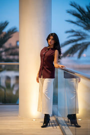 Woman wearing a maroon crepe vest with three front buttons and white wide-leg pants on a balcony at dusk