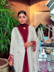 Woman wearing Harir Kubra Ivory Abaya with burgundy embroidery on sleeves and front edges in elegant indoor setting