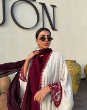 Woman wearing Harir Kubra Ivory Abaya with burgundy embroidery on sleeves and front edges in elegant indoor setting