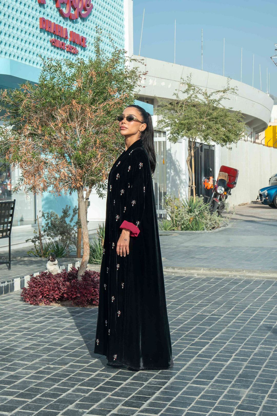 Black velvet abaya with delicate hand embroidery and maroon cuffs modeled outdoors