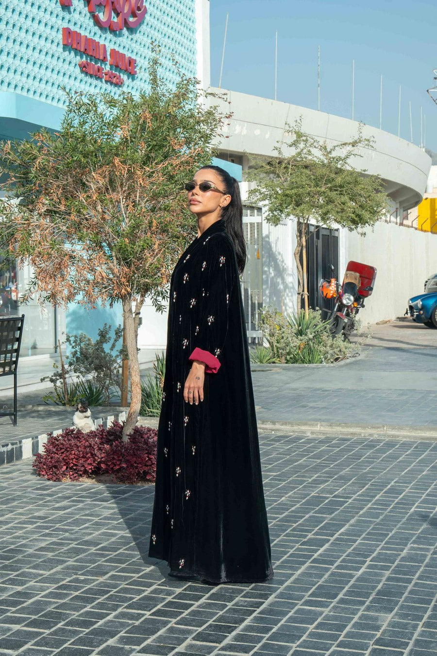 Black velvet abaya with delicate hand embroidery and maroon cuffs modeled outdoors