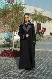 Woman wearing black crepe abaya with grey lapels and cuffs in urban outdoor setting