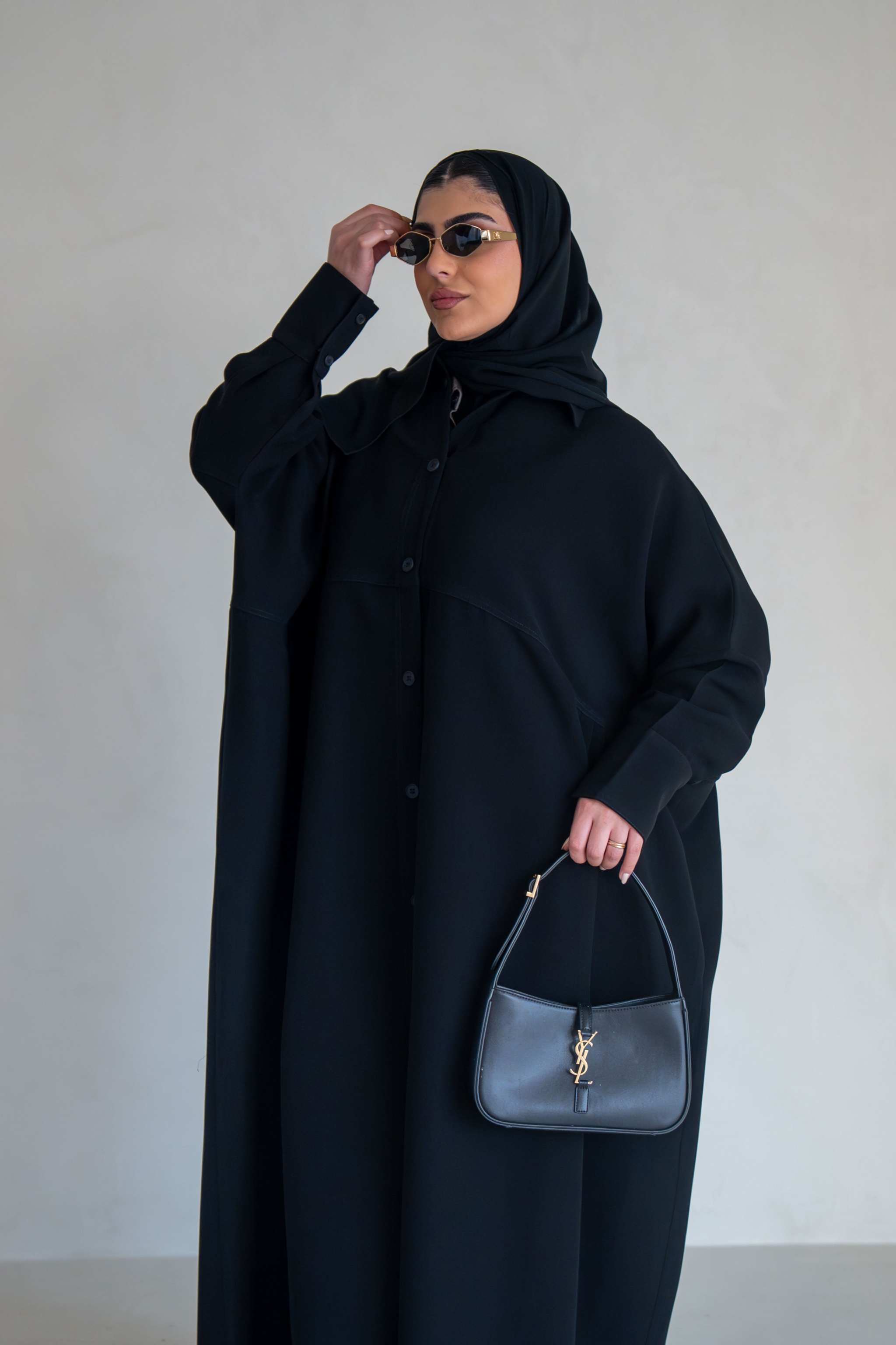 woman wearing free-size black abaya with loose flowy silhouette holding black handbag and wearing sunglasses