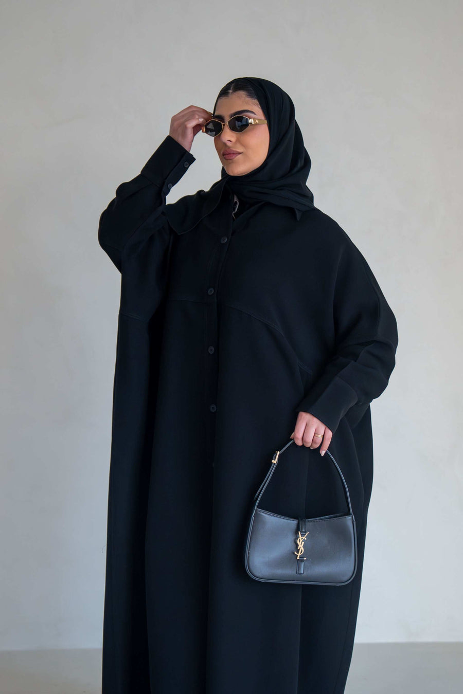 woman wearing free-size black abaya with loose flowy silhouette holding black handbag and wearing sunglasses