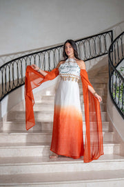 Woman wearing Tangerine Ombre cold-shoulder ombré dress with dramatic cape sleeves and hand embroidery on staircase