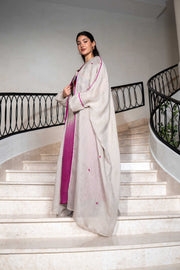 Woman wearing elegant beige and magenta ombre one-piece with floral embroidery and lightweight bisht with magenta piping on staircase