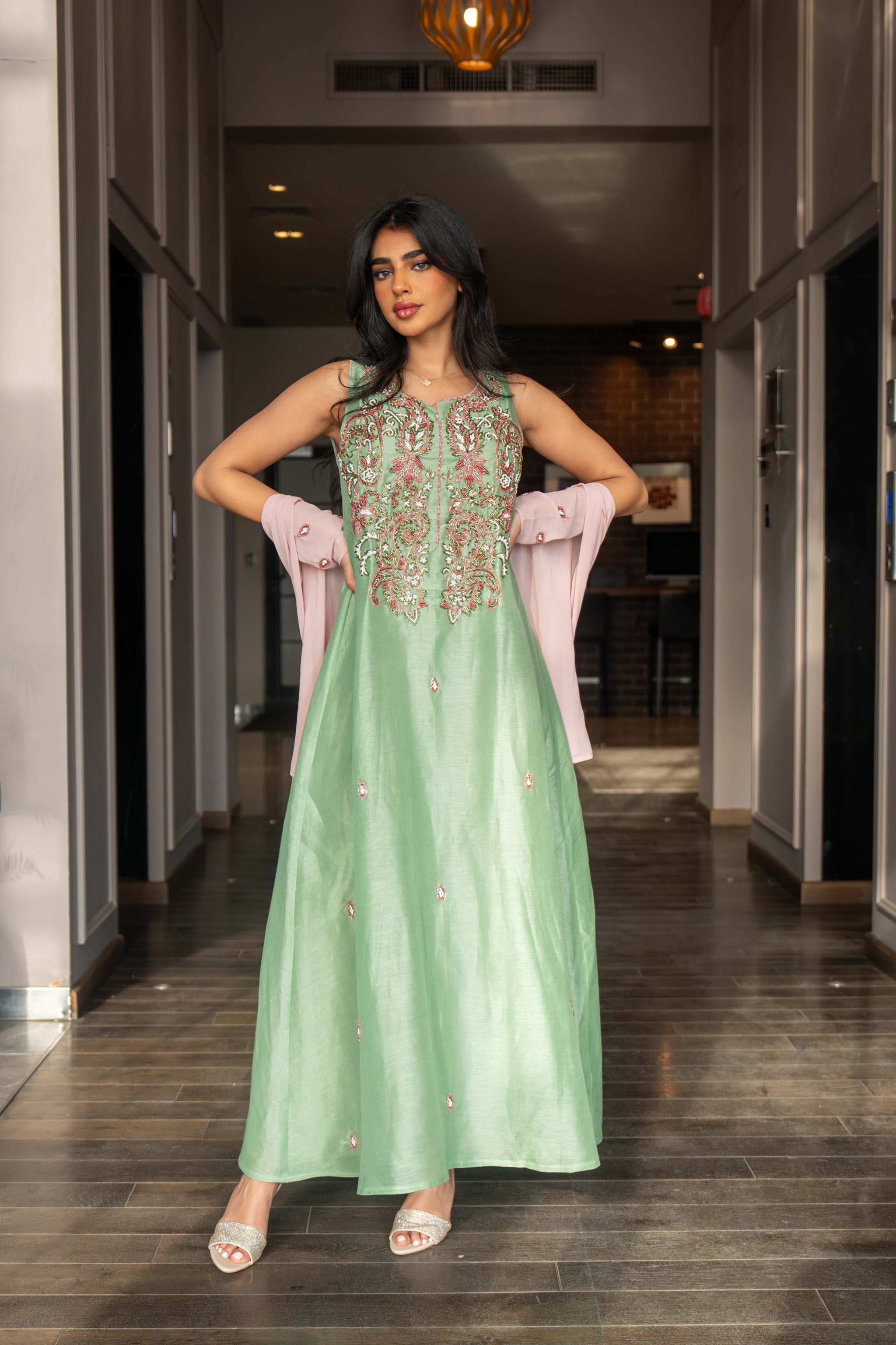 woman wearing pastel green one-piece dress with floral embroidery and blush pink cape sleeves standing indoors