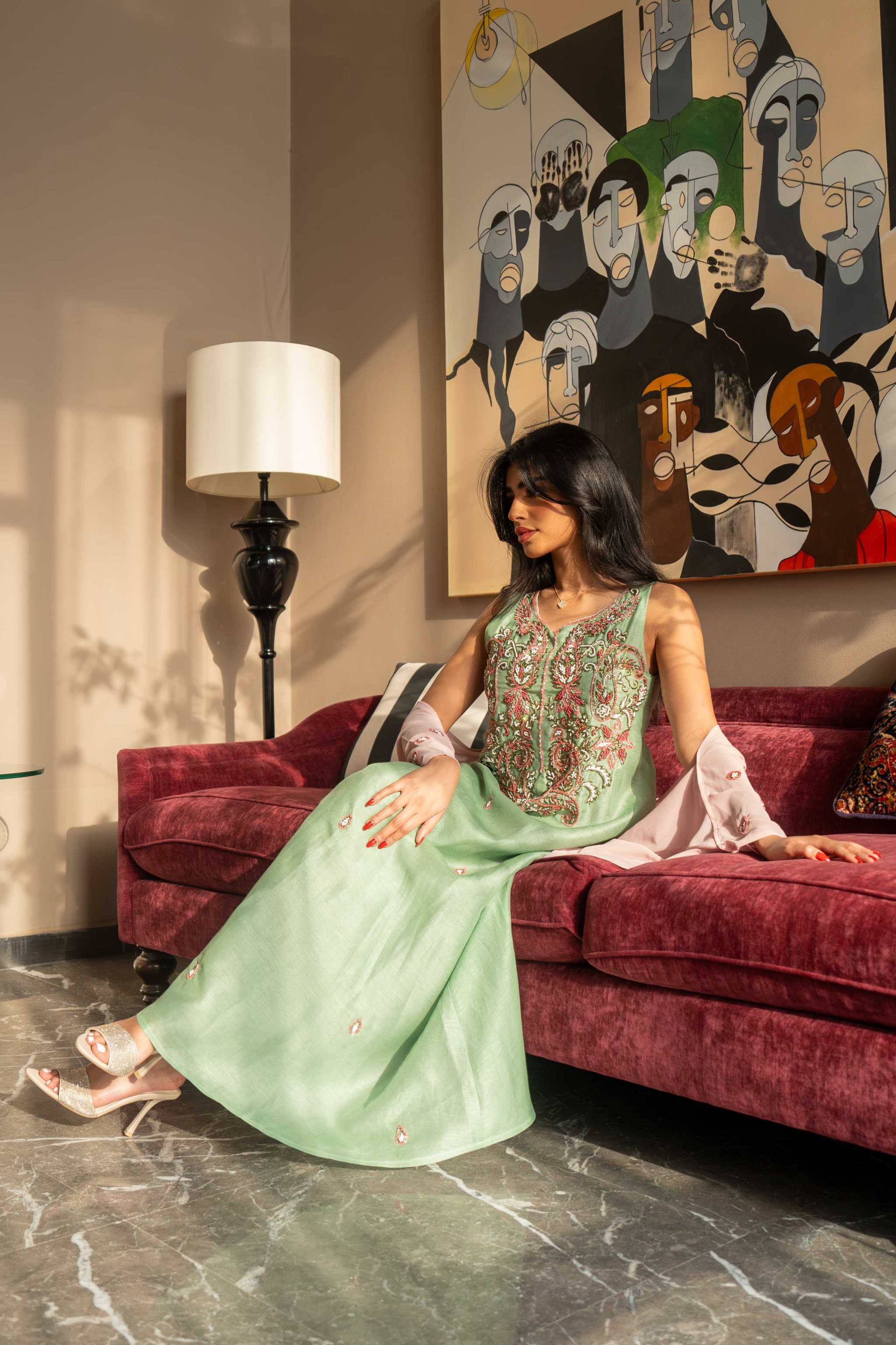 soft pastel green one-piece dress with floral embroidery and blush pink cape sleeves sitting on maroon sofa