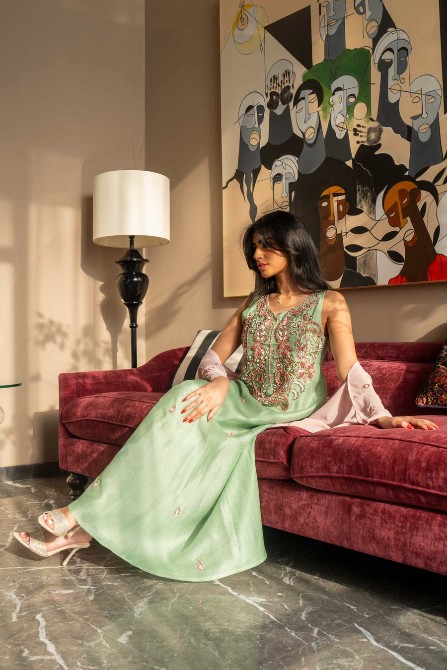 soft pastel green one-piece dress with floral embroidery and blush pink cape sleeves sitting on maroon sofa