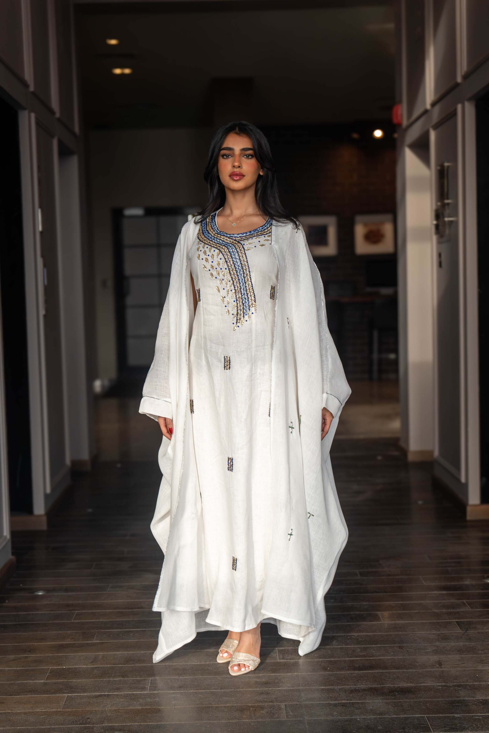 Woman wearing a refined white dress with blue embroidered neckline and soft asymmetric bisht with minimal embroidery