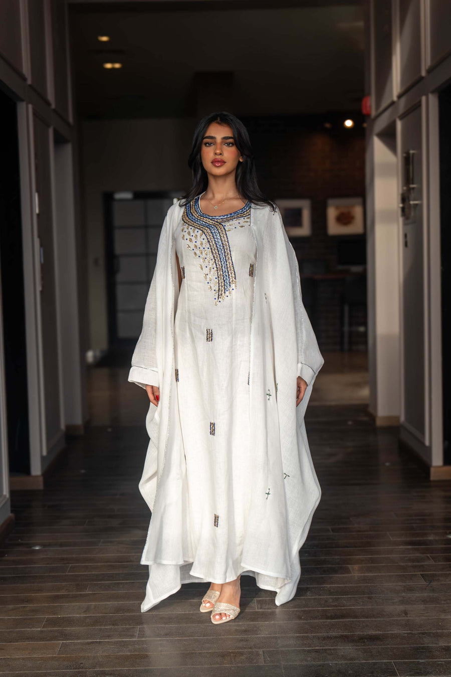 Woman wearing a refined white dress with blue embroidered neckline and soft asymmetric bisht with minimal embroidery