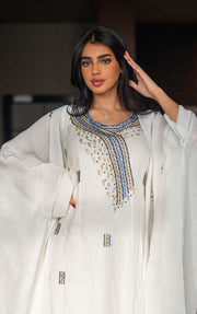 Woman wearing a refined white dress with blue embroidered neckline and soft asymmetric bisht with minimal embroidery