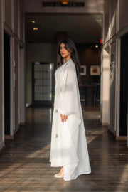 Woman wearing a refined white dress with blue embroidered neckline and soft asymmetric bisht with minimal embroidery