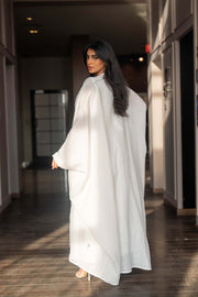 Woman wearing a refined white dress with blue embroidered neckline and soft asymmetric bisht with minimal embroidery