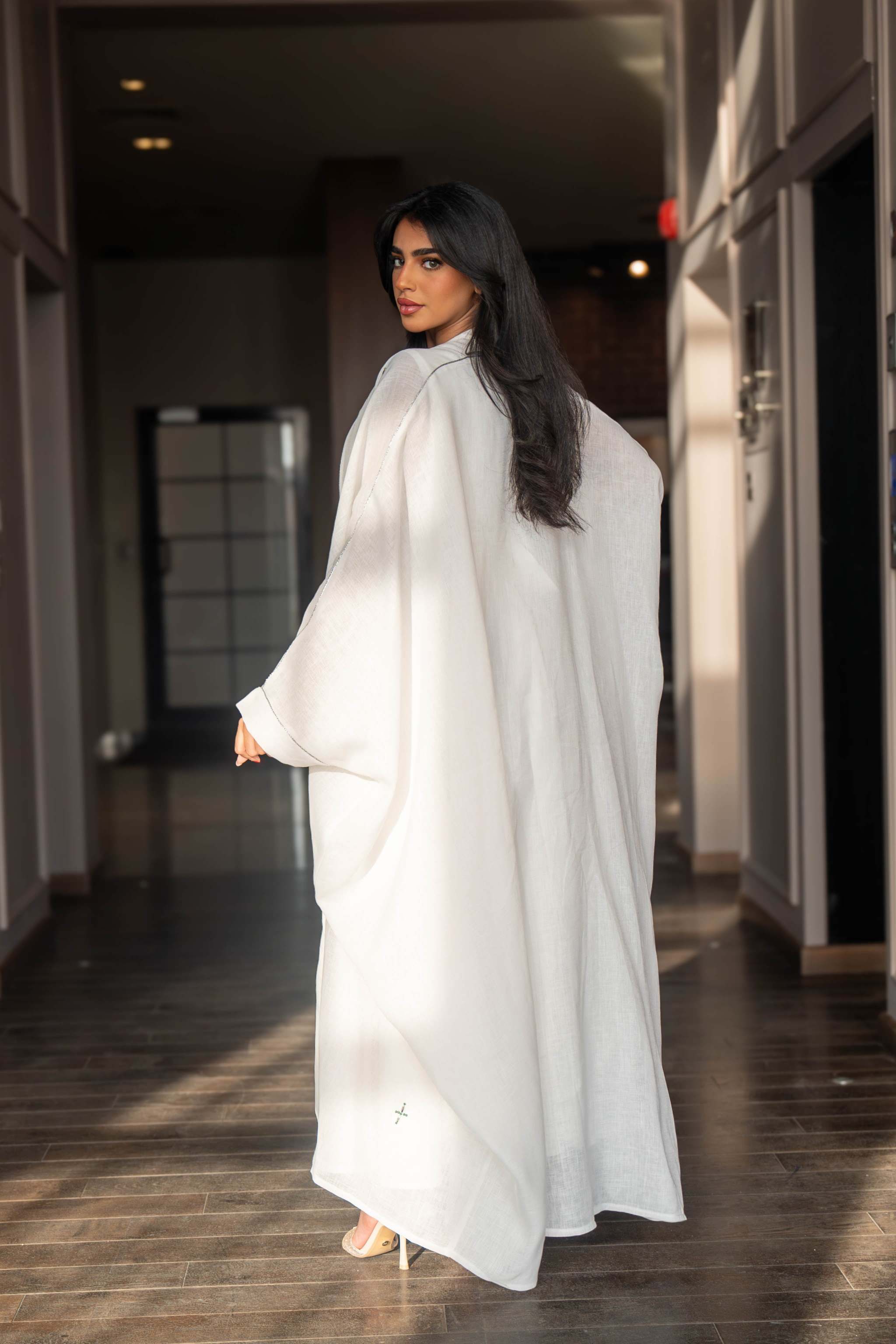 Woman wearing a refined white dress with blue embroidered neckline and soft asymmetric bisht with minimal embroidery