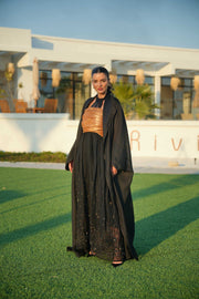 Woman wearing Golden Touch ensemble featuring black bisht with golden embroidery and black to gold gradient linen jumpsuit outdoors on grass