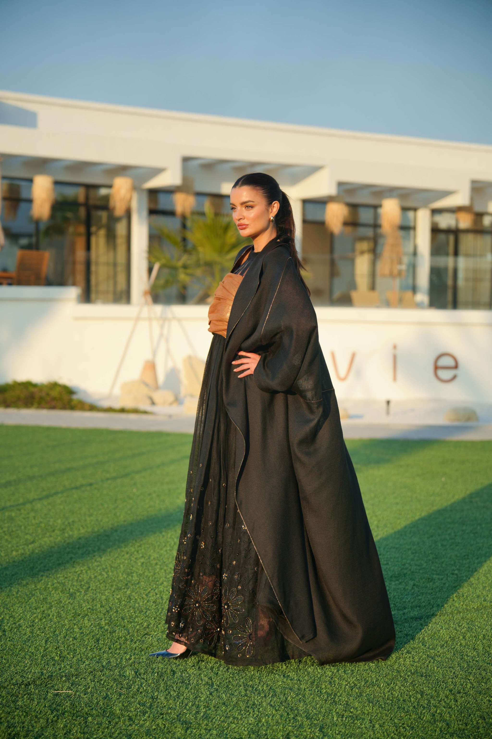 Woman wearing a black khesha bisht with golden touch embroidery paired with a black to golden linen jumpsuit featuring subtle golden details, styled outdoors.