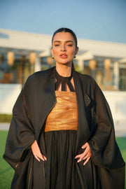 Woman wearing a black khesha bisht with golden touch embroidery paired with a black to golden linen jumpsuit featuring subtle golden details, styled outdoors.