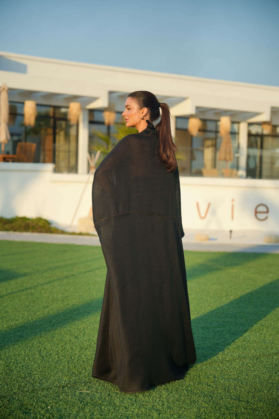 Woman wearing a black khesha bisht with golden touch embroidery paired with a black to golden linen jumpsuit featuring subtle golden details, styled outdoors.