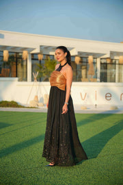 Woman wearing a black khesha bisht with golden touch embroidery paired with a black to golden linen jumpsuit featuring subtle golden details, styled outdoors.