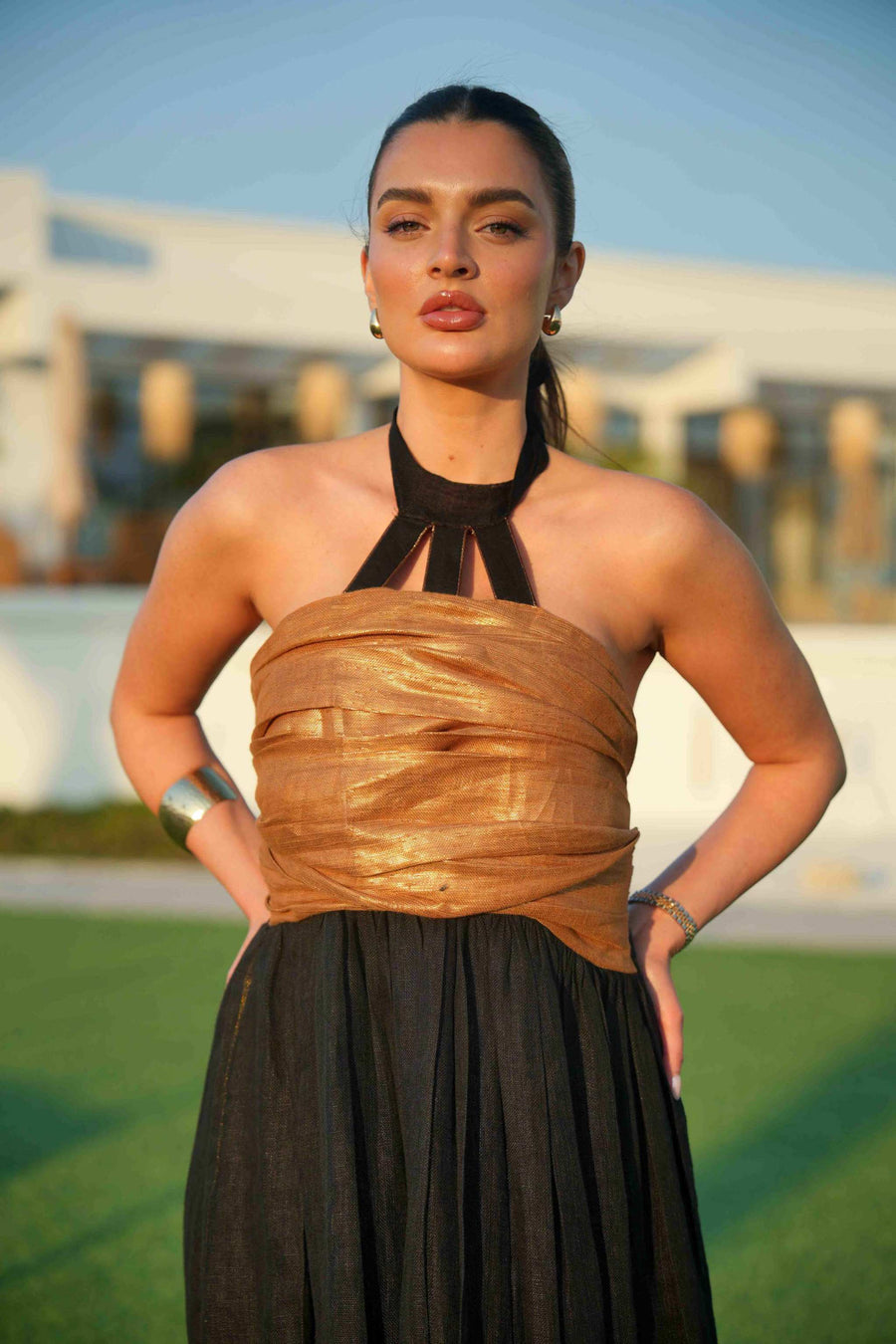 Woman wearing a black khesha bisht with golden touch embroidery paired with a black to golden linen jumpsuit featuring subtle golden details, styled outdoors.