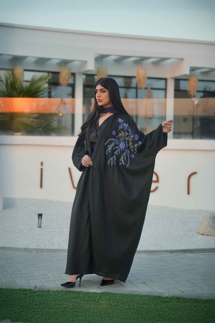luxurious black bisht with blue embroidery and mirrored details worn by woman outdoors