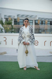woman wearing elegant white bisht with bold black Arabic calligraphy embroidery on sleeves and upper bodice standing outdoors