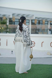 woman wearing elegant white bisht with bold black Arabic calligraphy embroidery on sleeves and upper bodice standing outdoors