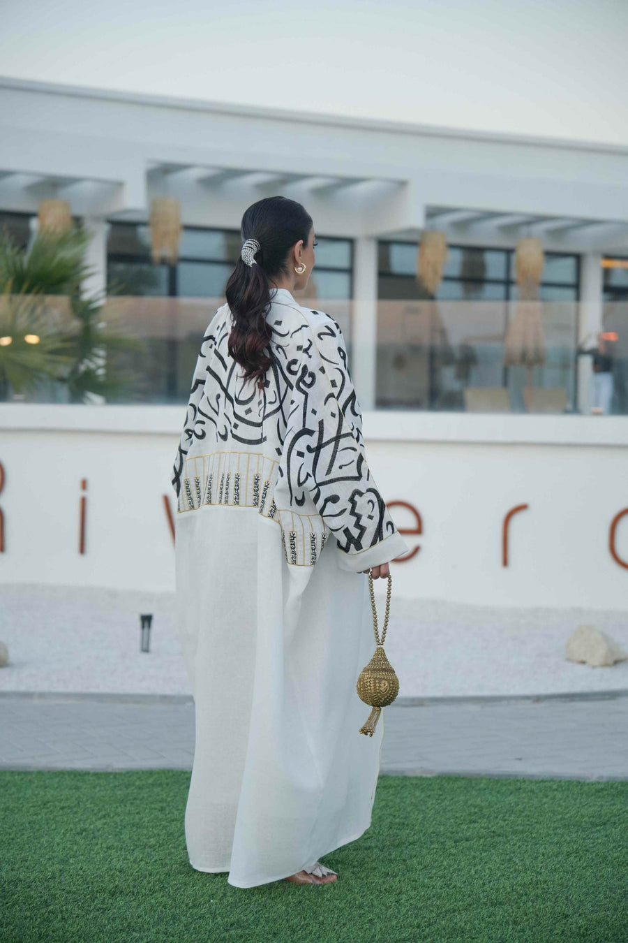 woman wearing elegant white bisht with bold black Arabic calligraphy embroidery on sleeves and upper bodice standing outdoors