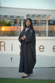 luxurious black bisht with blue embroidery and mirrored details worn by woman outdoors