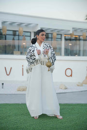 woman wearing elegant white bisht with bold black Arabic calligraphy embroidery on sleeves and upper bodice standing outdoors