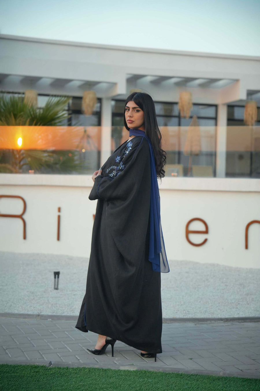 luxurious black bisht with blue embroidery and mirrored details worn by woman outdoors