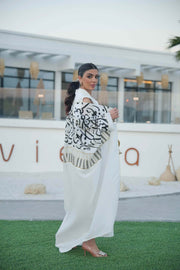 woman wearing elegant white bisht with bold black Arabic calligraphy embroidery on sleeves and upper bodice standing outdoors