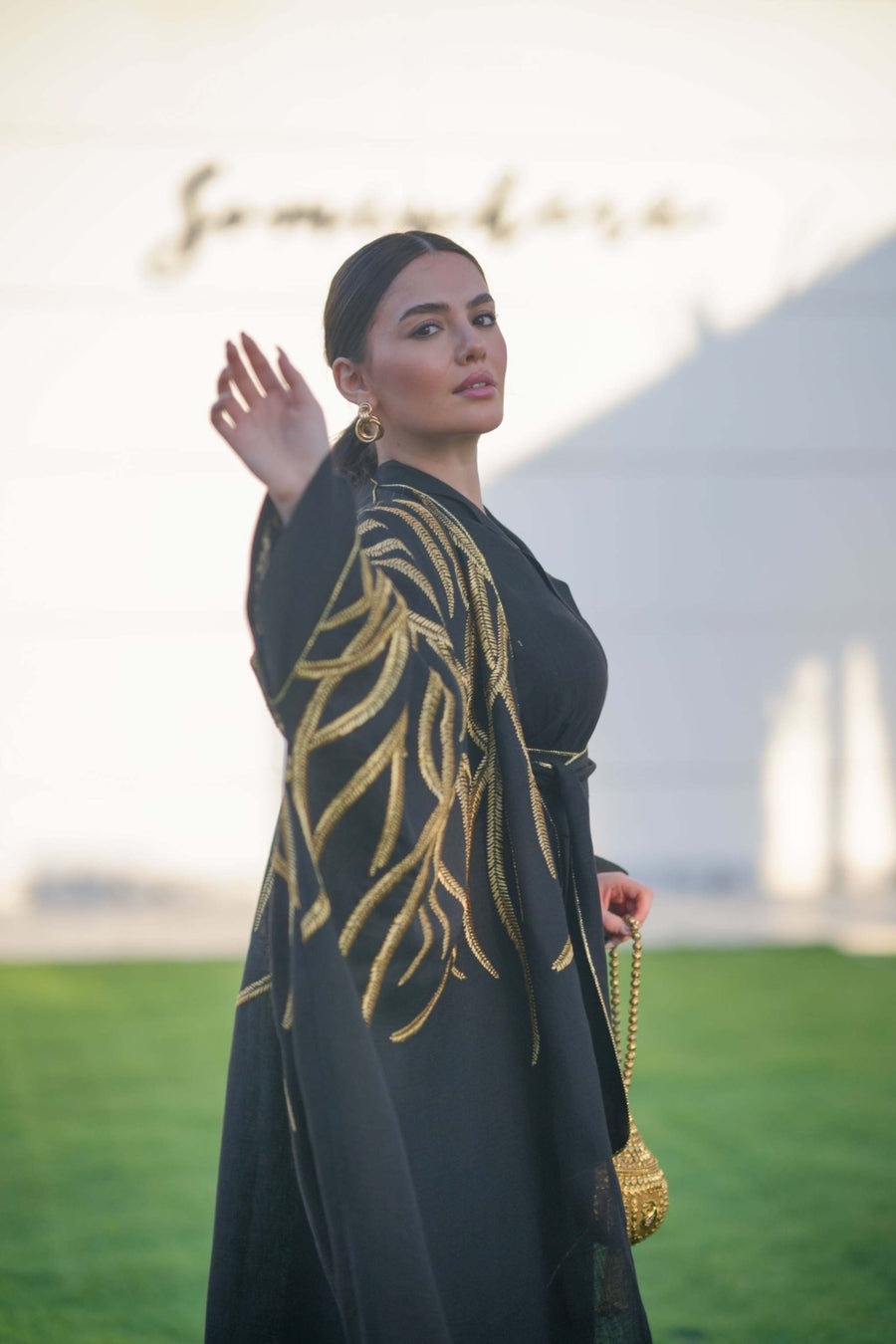 Black linen bisht with bold gold leaf embroidery and wide sleeves, styled over elegant eveningwear.