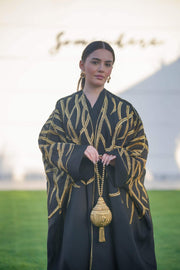 Black linen bisht with wide sleeves and bold gold leaf embroidery, styled for elegant layering and special occasions.