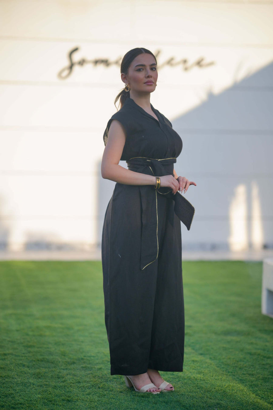 Woman wearing a sleek black linen jumpsuit with a cinched waist and wide-leg cut standing outdoors on grass.