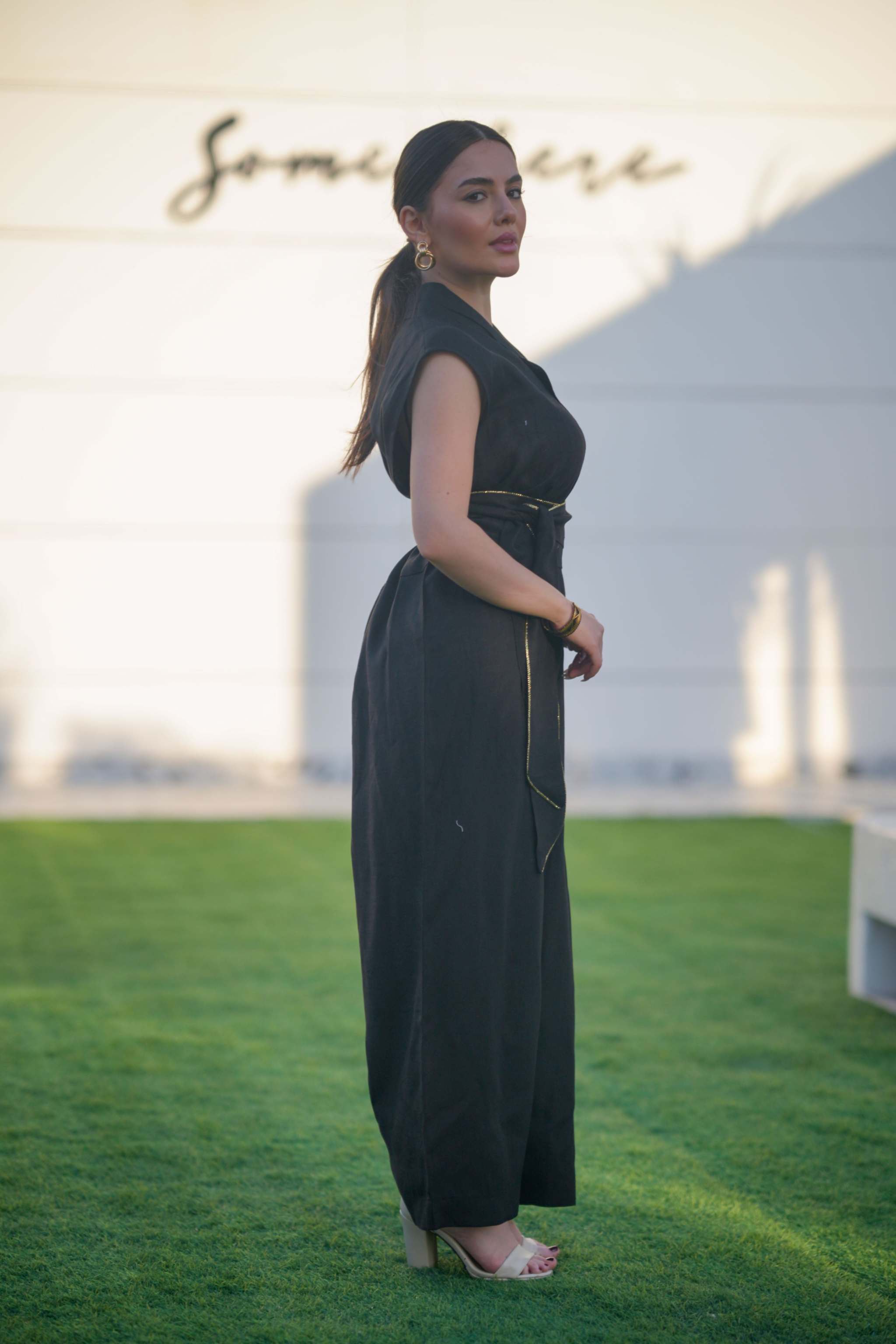 Woman wearing a sleeveless black linen jumpsuit with a cinched waist and wide legs standing outdoors on grass