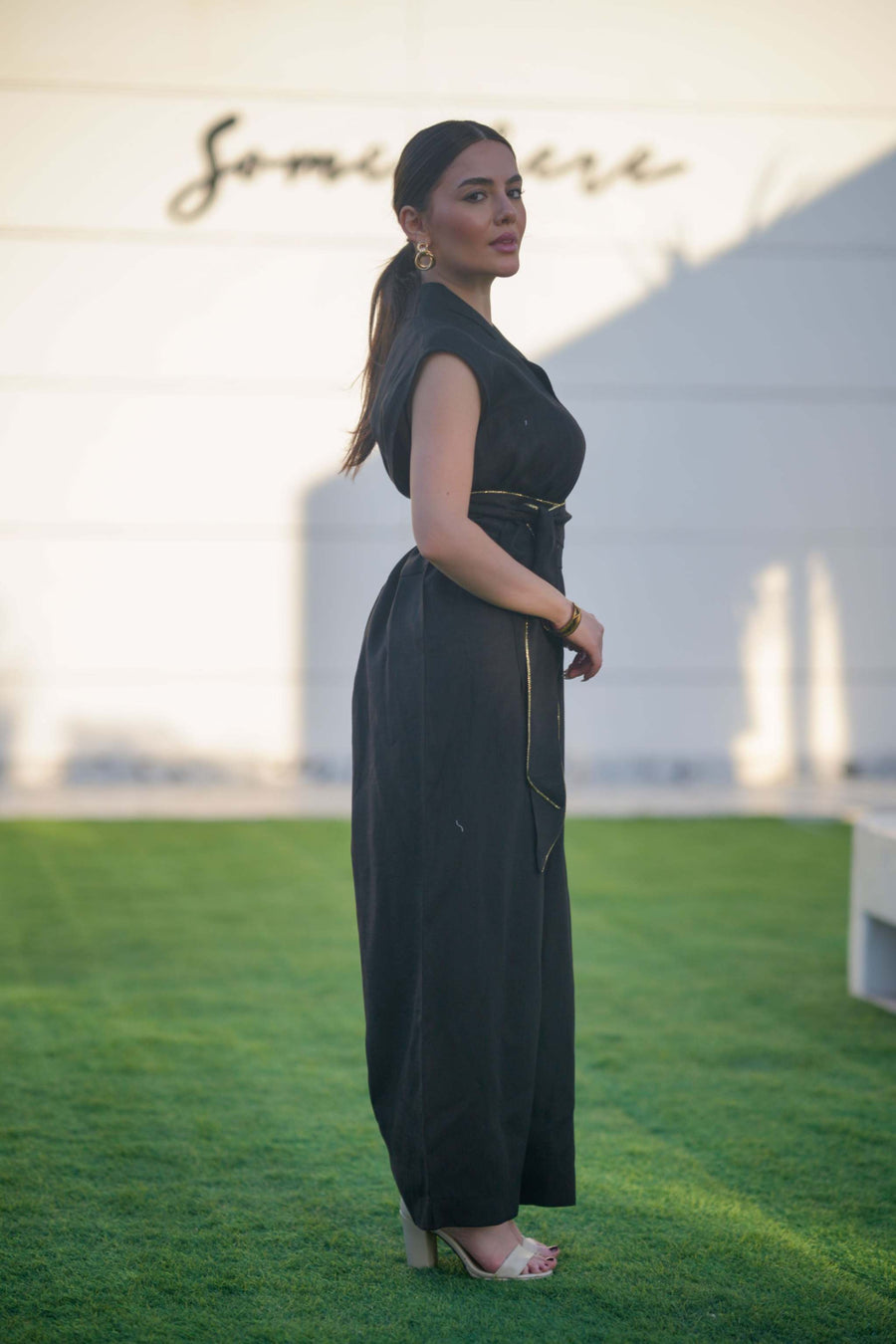 Woman wearing a sleeveless black linen jumpsuit with a cinched waist and wide legs standing outdoors on grass