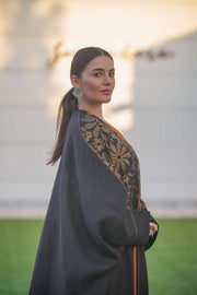 Elegant black bisht with golden floral embroidery and wide sleeves layered over a rust-colored jumpsuit
